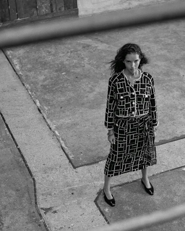 Woman in a black and white patterned two-piece outfit stands on a concrete surface in a fashion editorial style photograph.