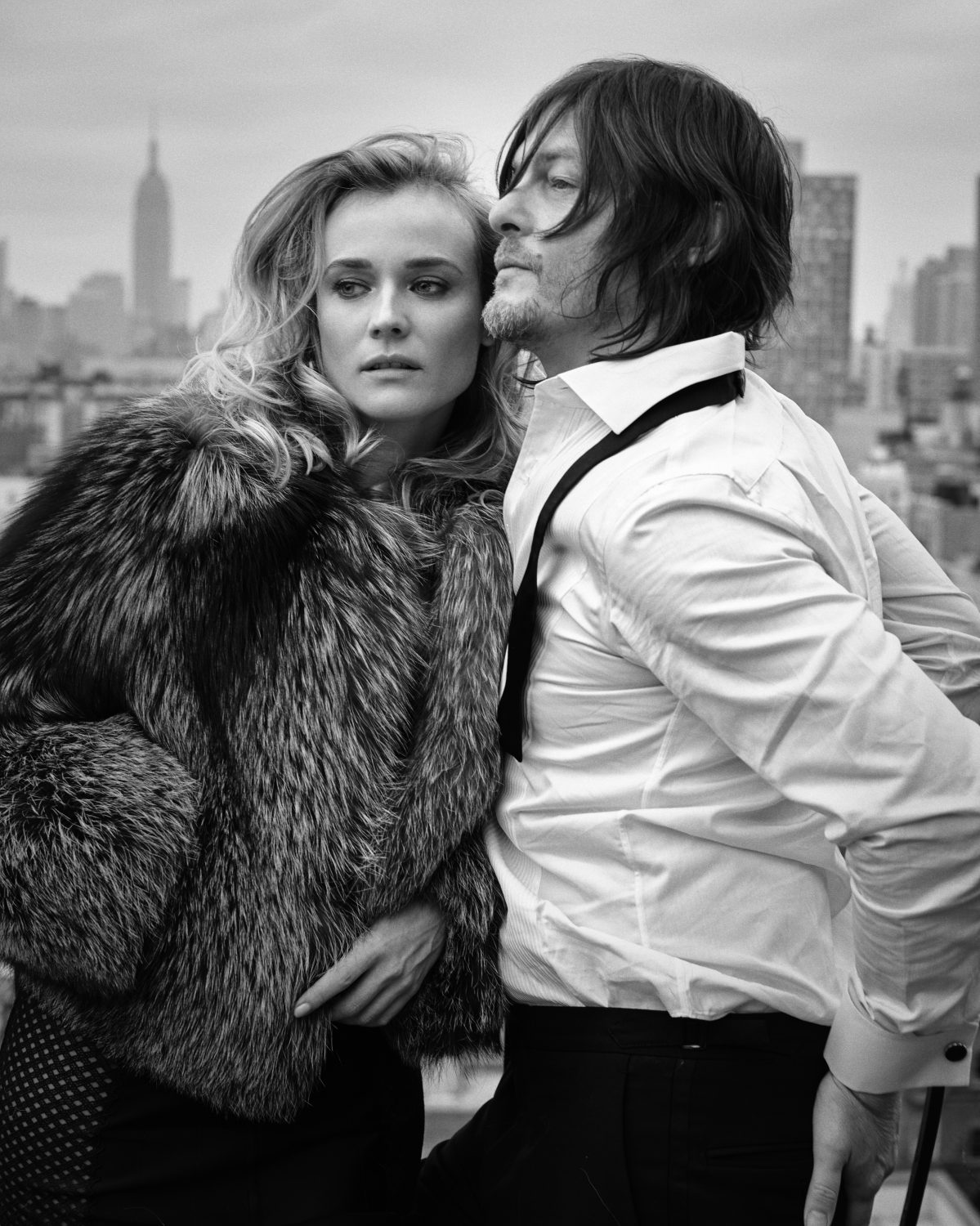Black and white portrait of a celebrity couple, a blonde woman in a fur coat and a man with long hair, standing on a rooftop in New York City.