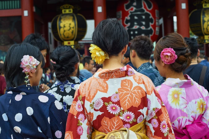 Group of people wearing colourful traditional yukata robes with floral hair ornaments seen from behind at a shrine.