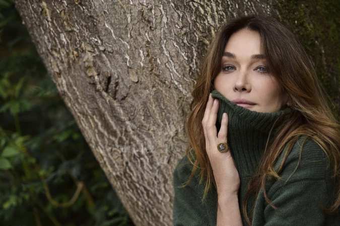 Woman in dark green turtleneck sweater leaning against a tree trunk in a woodland setting