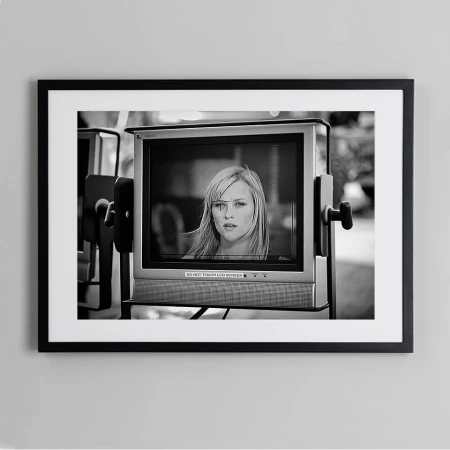 Black and white photograph of a television monitor displaying a woman with blonde hair and a serious expression, set against an outdoor background.