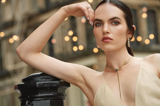 Model wearing a gold snake necklace and drop earrings posing outdoors with bokeh streetlights