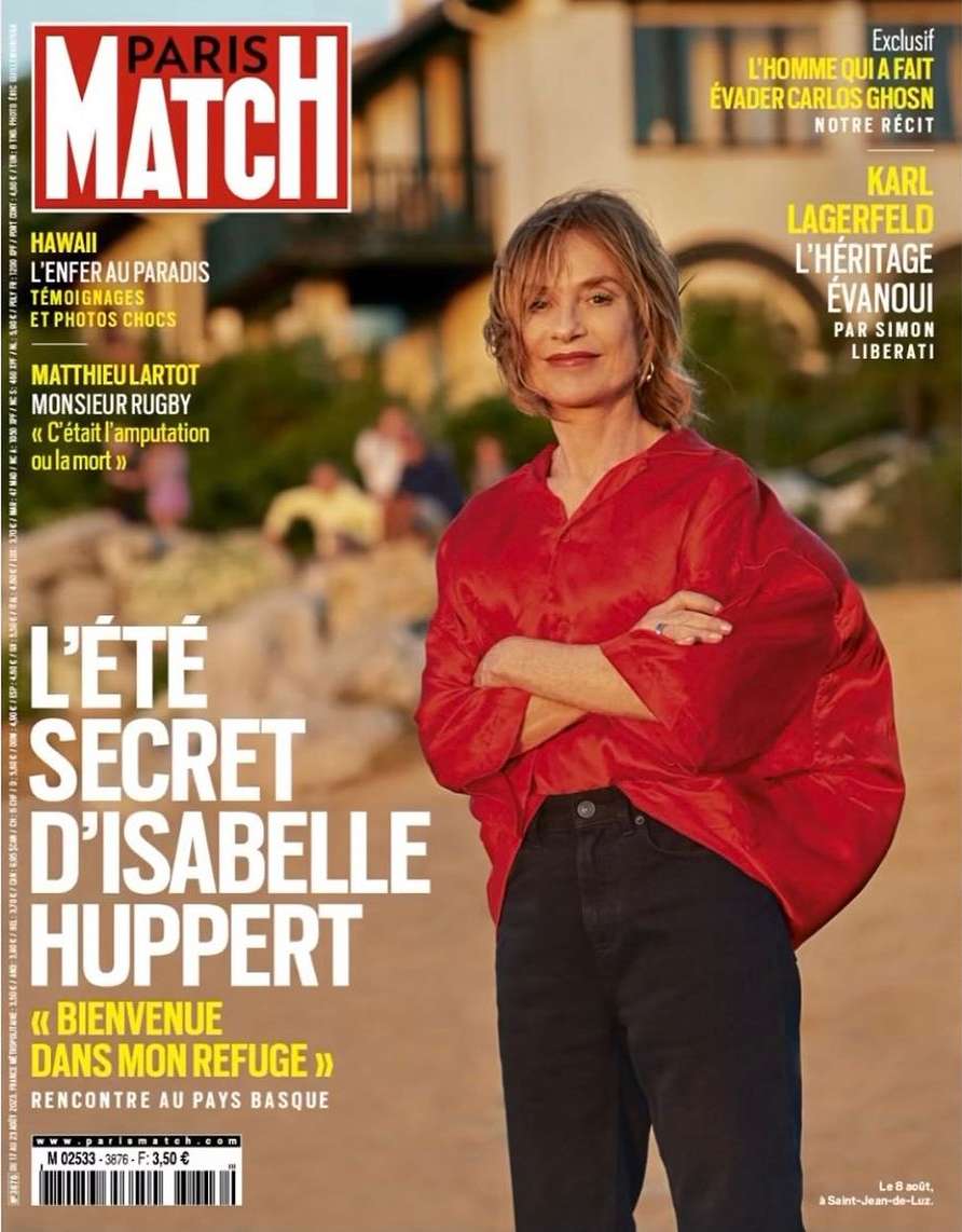 Magazine cover featuring Isabelle Huppert in a red shirt against a beach backdrop with architectural elements, and bold text overlay.