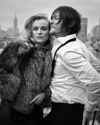 Black and white portrait of Diane Kruger and Norman Reedus posing outdoors on a rooftop with a city skyline backdrop.