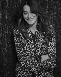 Monochrome portrait of a smiling woman with long hair wearing a leopard print blazer with crossed arms against a textured dark background.