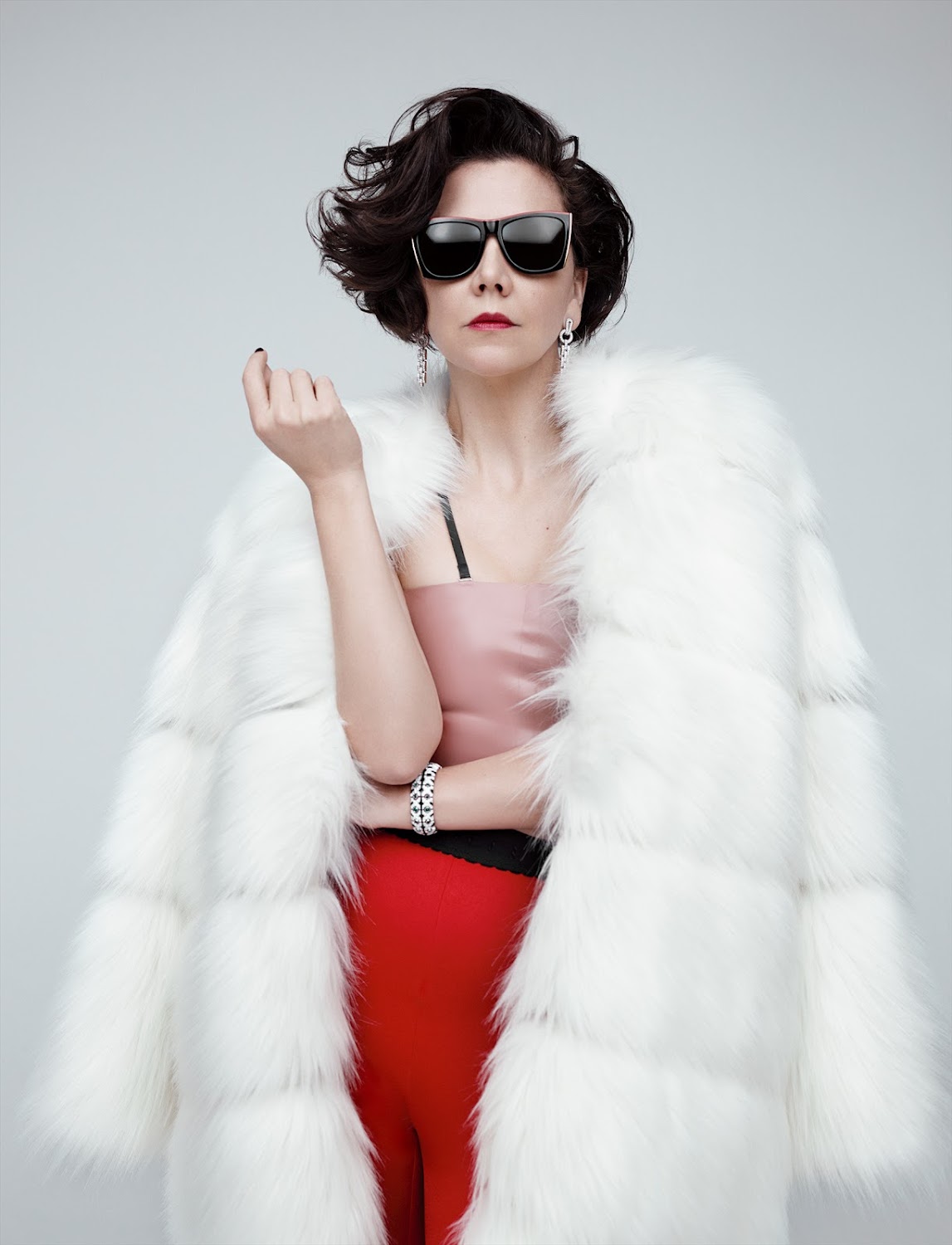 Stylish woman in a white faux fur coat and sunglasses poses against a neutral grey background in a studio portrait. Fashion editorial.