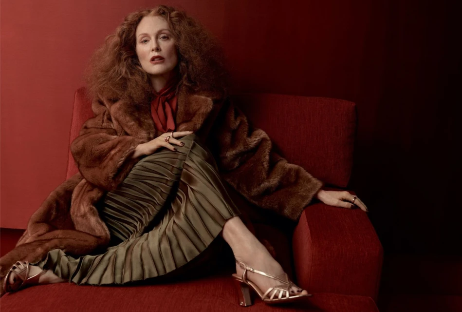 Portrait of a red-haired woman in a brown fur coat seated on a red chair, showcasing fashion and a relaxed pose in an indoor setting.