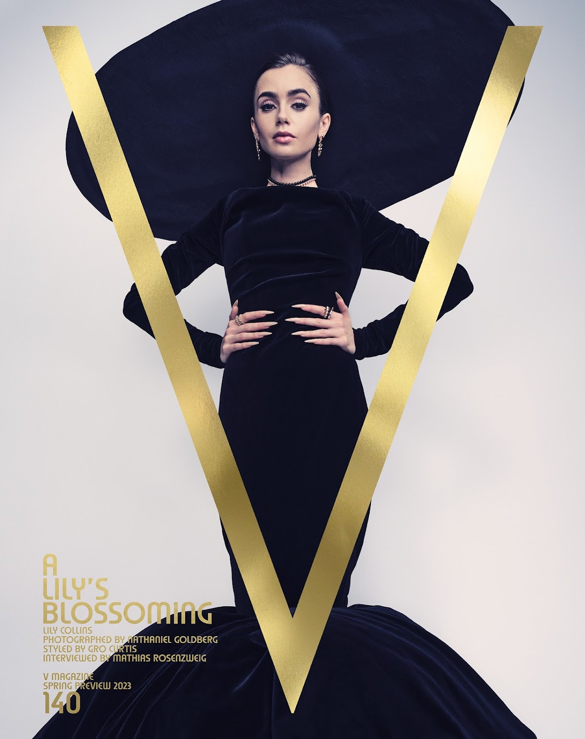 Lily Collins poses in a black dress and oversized hat with a gold "V" on a magazine cover against a light background. 