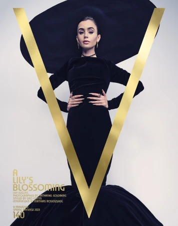 Lily Collins poses in a black dress and oversized hat with a gold "V" on a magazine cover against a light background. 