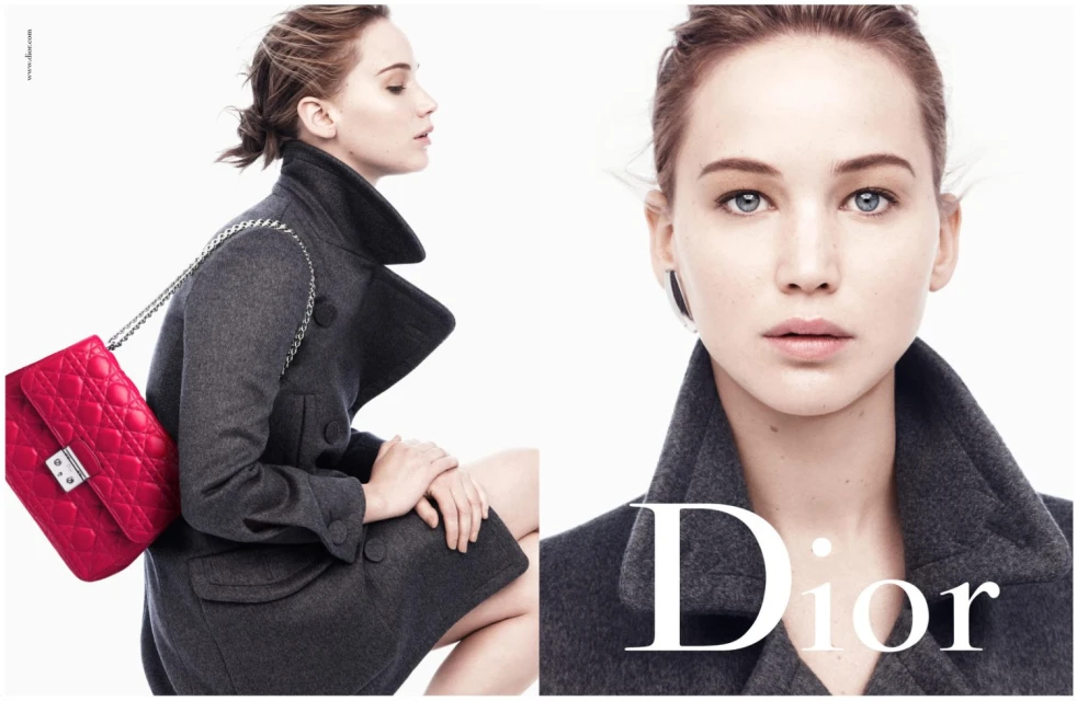 Jennifer Lawrence for Dior: an adult woman in a grey coat holding a red purse poses in front of a bright white background.