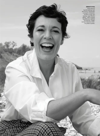 Black and white portrait of a laughing woman wearing a white collared shirt and plaid pants outdoors near water.