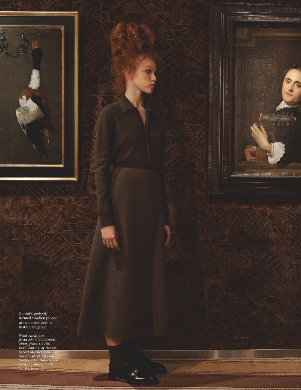 A woman with dark hair and red lips poses in a photo studio, wearing a black turtleneck and a serious expression.