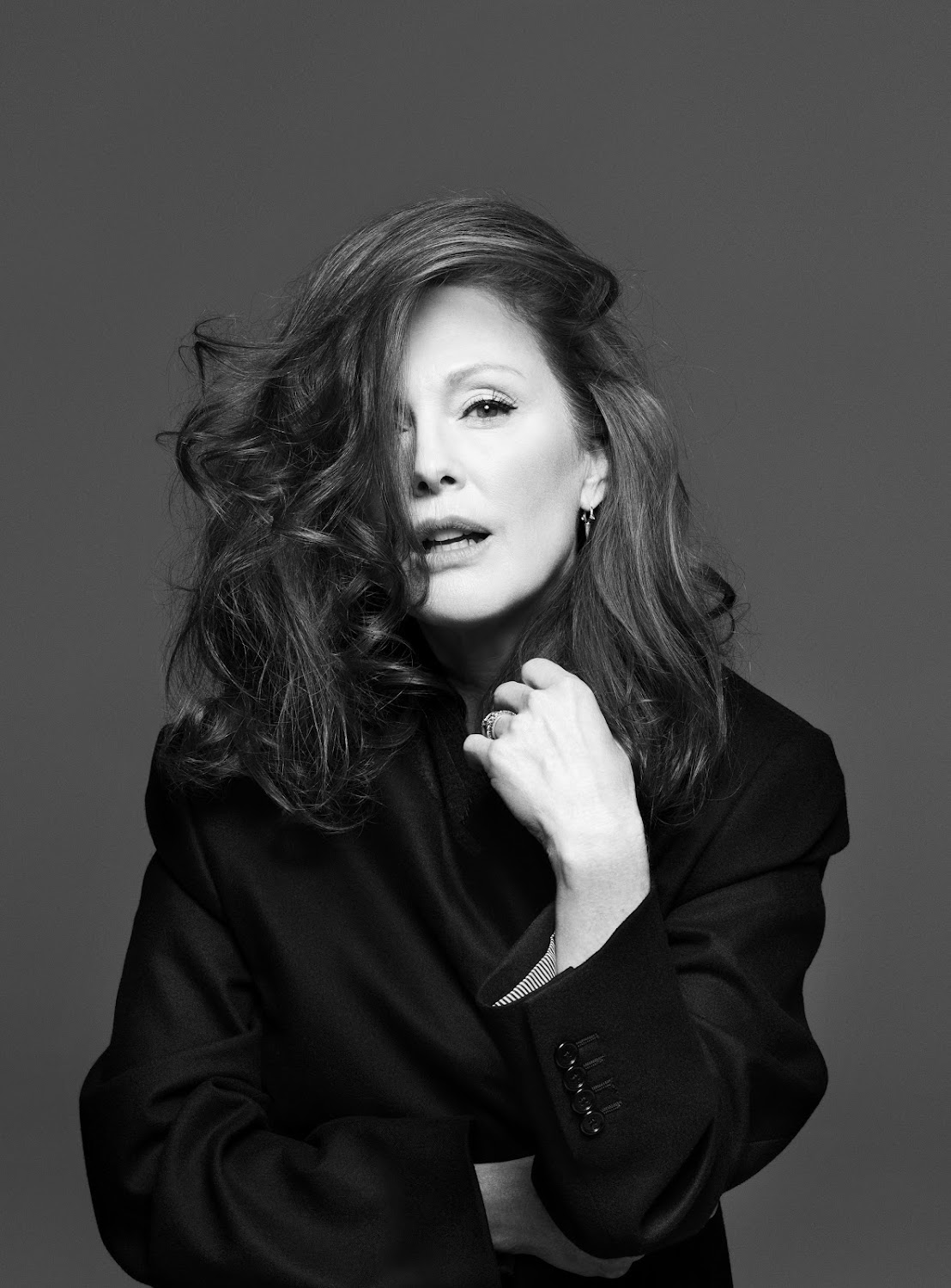 Portrait of a woman with voluminous dark hair and black blazer against a grey backdrop featuring make-up by Francelle Daly