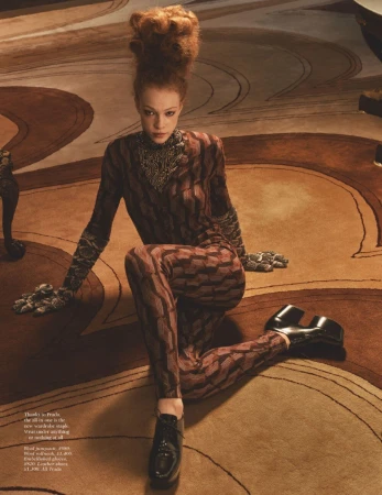 A female fashion model with a high auburn beehive hairstyle poses in a patterned jumpsuit and platform shoes on a patterned carpet.