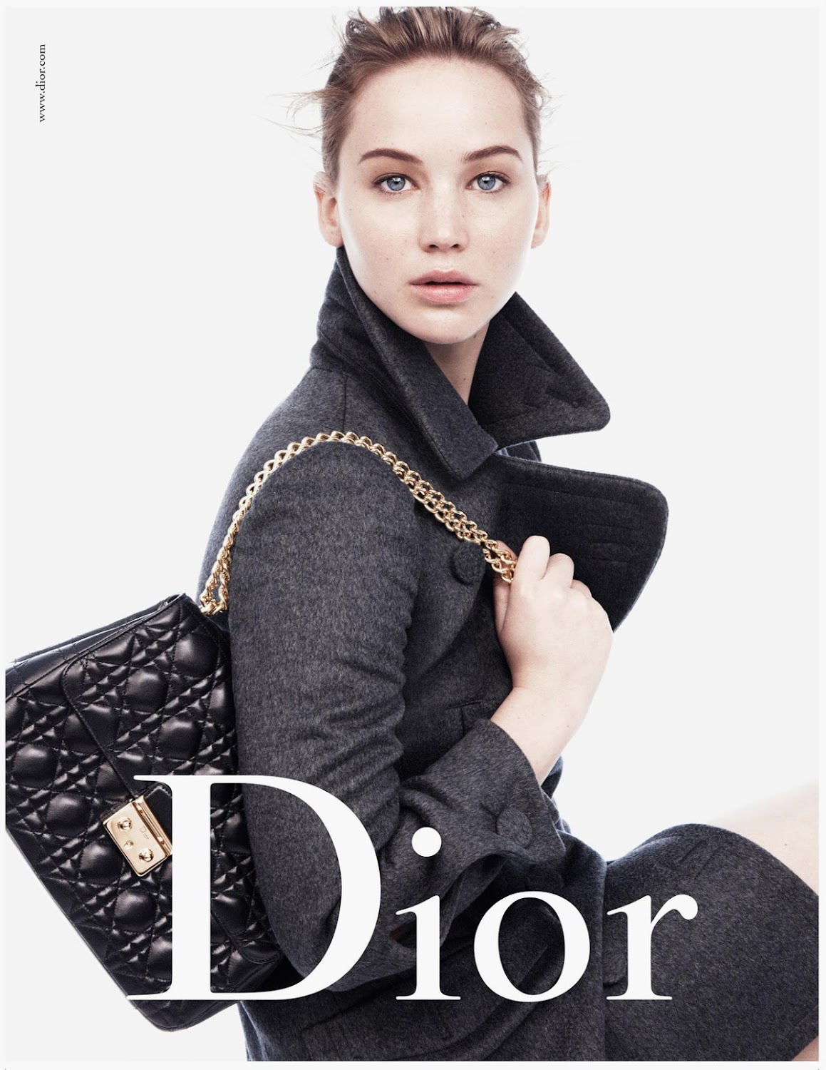 Jennifer Lawrence poses with a black quilted Dior bag and grey wool coat against a white background in a fashion editorial shot.