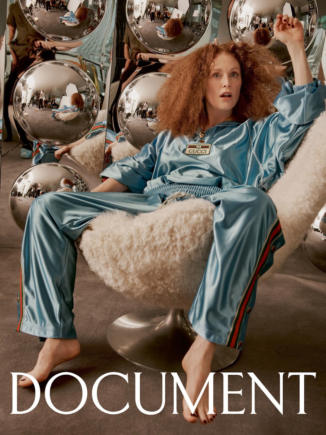 Julianne Moore sits in a silver swivel chair wearing a blue track suit with red stripes against a background of mirrored spheres.