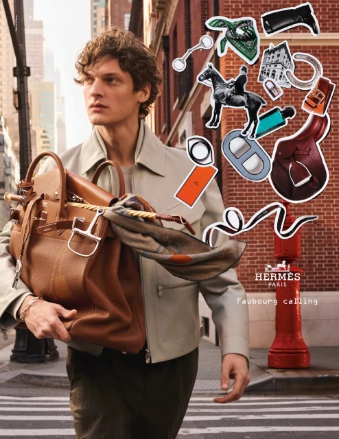 Male model carries a brown leather bag in a city street with Hermes-themed cartoon stickers in the background. Fashion advertising.