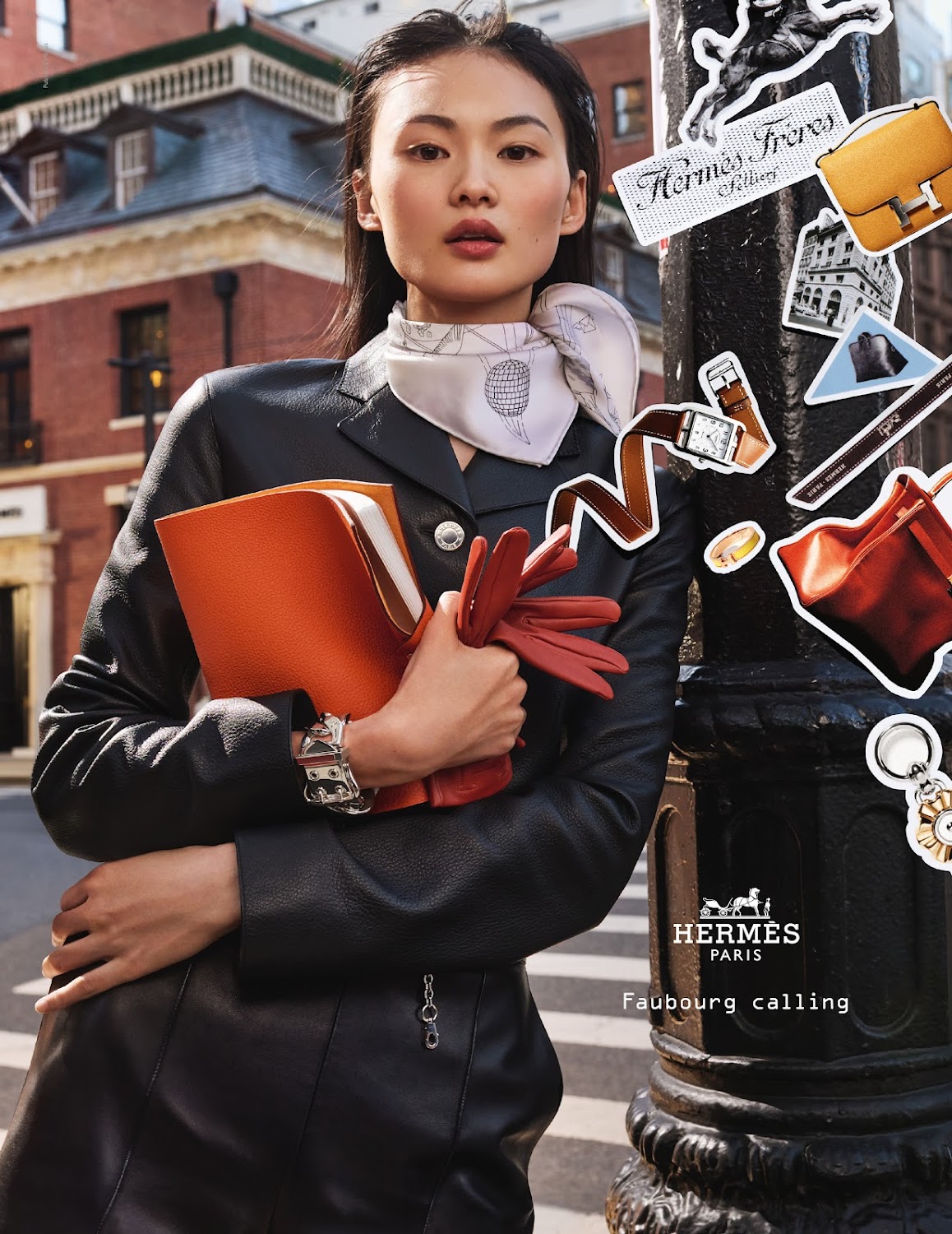 Elegant Asian woman in a black leather suit holds an orange document case and gloves, leaning against a lamp post in an urban setting.
