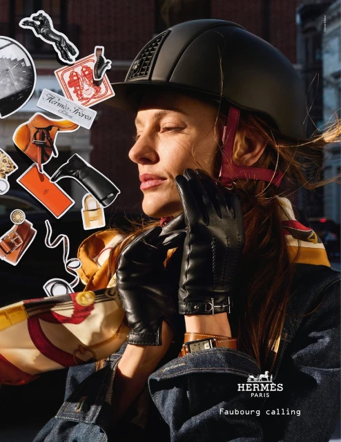 Equestrian-style fashion shot of a woman in a riding helmet and denim jacket, accessorized with black gloves, scarves, and jewelry, outdoors.