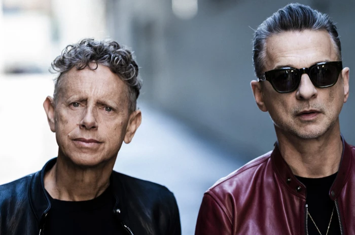 Portrait of two men, one in a red leather jacket wearing sunglasses and another with curly grey hair in a dark jacket.