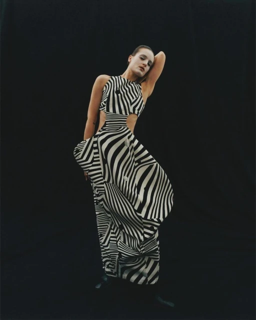 A stylish adult woman in a zebra-striped dress poses in a studio. The woman stands in front of a dark background.