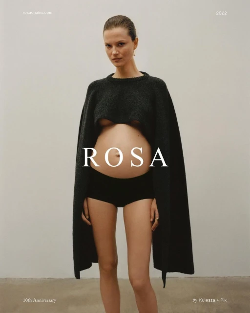 Portrait of pregnant woman in black knitwear, black bottoms, and minimal makeup against a neutral background, showcasing fashion.