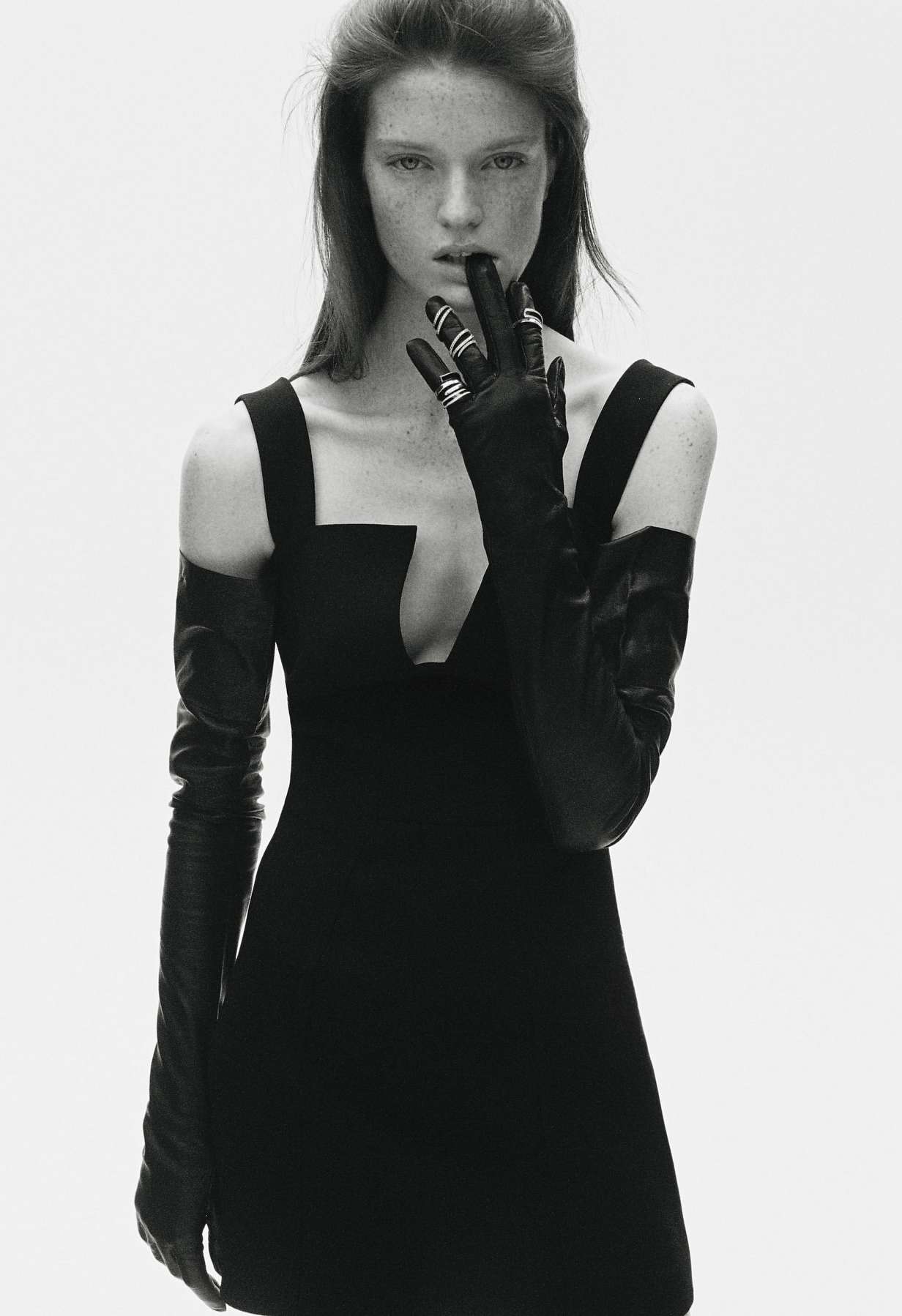 Monochromatic fashion shot: A woman with fair skin poses in a black dress and gloves against a bright white backdrop.