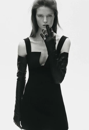 Monochromatic fashion shot: A woman with fair skin poses in a black dress and gloves against a bright white backdrop.