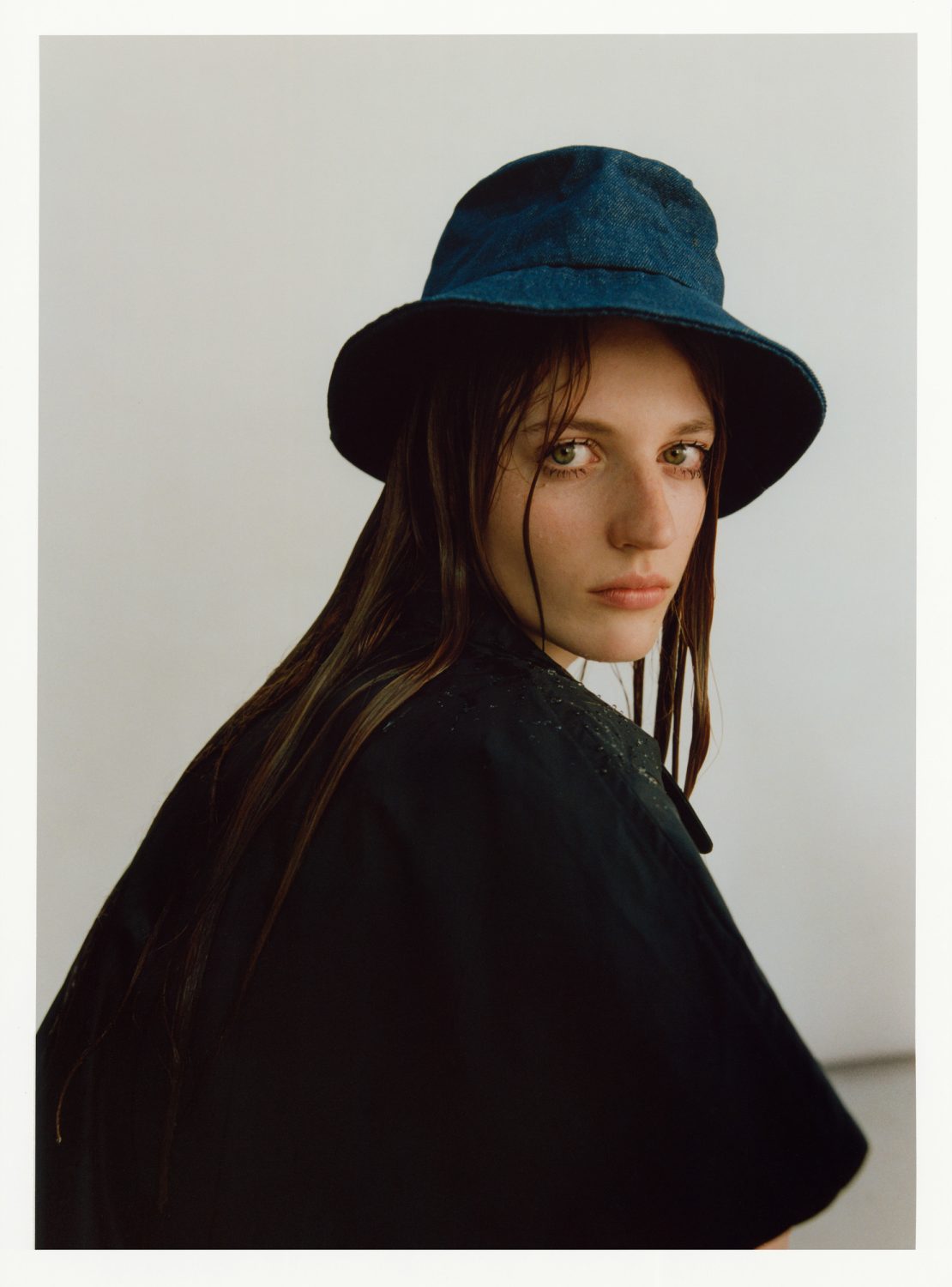 Portrait of a woman with long brown hair wearing a dark blue bucket hat and black jacket, posing in front of a neutral background.