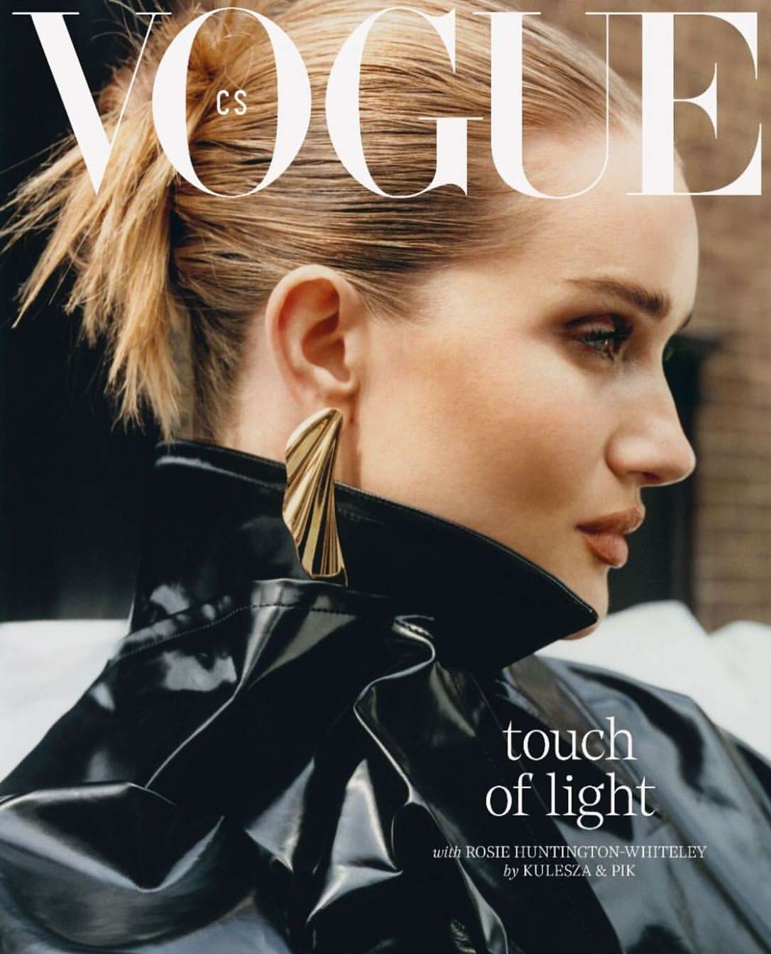 Close-up of Rosie Huntington-Whiteley in a Vogue cover wearing a black patent leather jacket and large gold earrings, side profile.