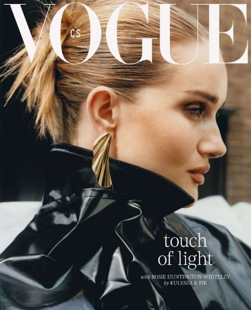 Close-up of Rosie Huntington-Whiteley in a Vogue cover wearing a black patent leather jacket and large gold earrings, side profile.