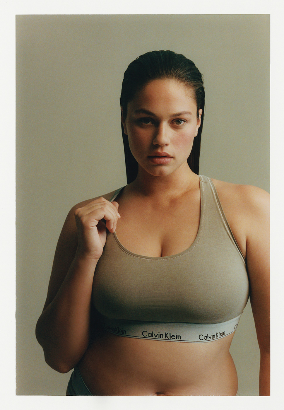 Adult woman posing in a Calvin Klein sports bra with fair skin and dark hair in a portrait, studio lighting and neutral background.