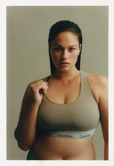 Adult woman posing in a Calvin Klein sports bra with fair skin and dark hair in a portrait, studio lighting and neutral background.