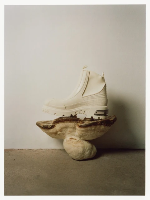 White boot is displayed on a stone pedestal against an off-white wall and concrete floor. Fashionable footwear still life product shot.