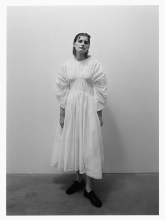 Model in a voluminous white puff-sleeve dress and dark shoes against a plain wall shot by Kulesza and Pik