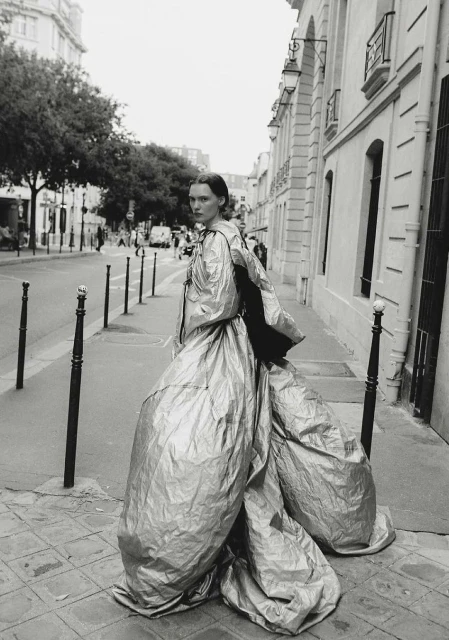 Fashion shot of adult woman in silver couture gown standing on a cobblestone street in front of buildings and street lights in black and white.