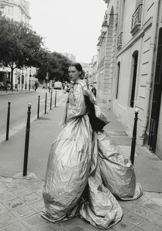 Fashion shot of adult woman in silver couture gown standing on a cobblestone street in front of buildings and street lights in black and white.