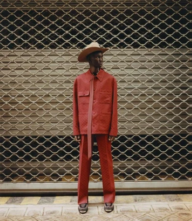 Man wearing a red patterned suit and straw cowboy hat standing in front of a metal rolling security shutter.