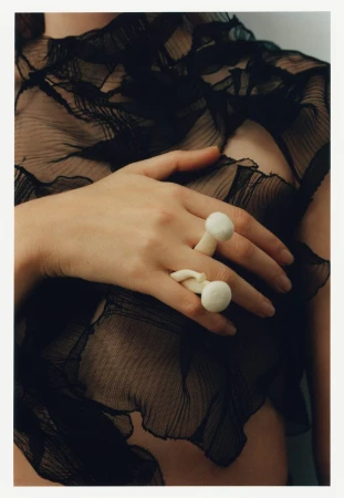 Close-up of a hand wearing white mushroom rings resting on a sheer black ruffled top by Kulesza and Pik.