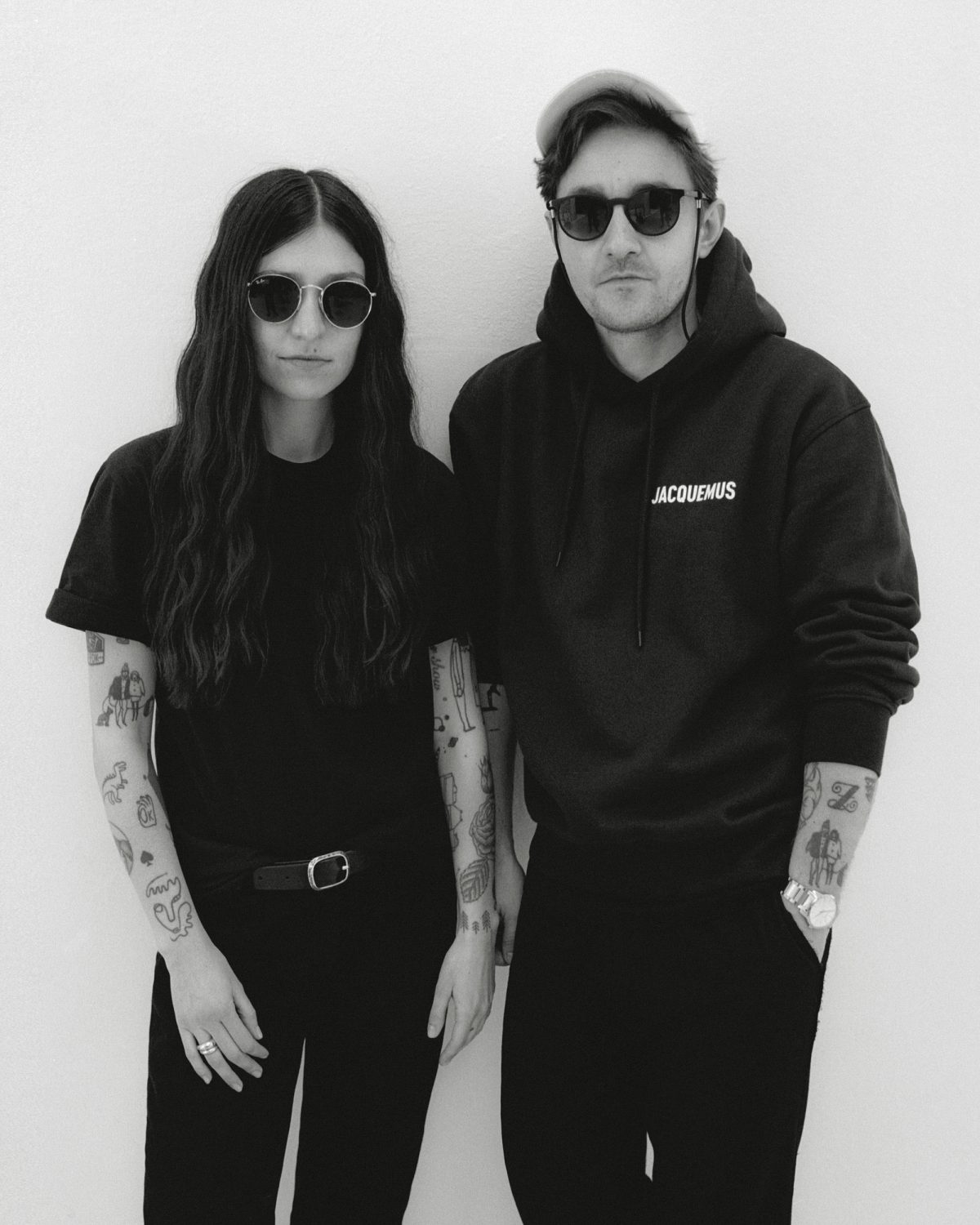 Portrait of a man and woman in black t-shirts and hoodies wearing sunglasses against a white background by Kulesza and Pik