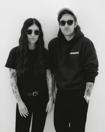 Portrait of a man and woman in black t-shirts and hoodies wearing sunglasses against a white background by Kulesza and Pik