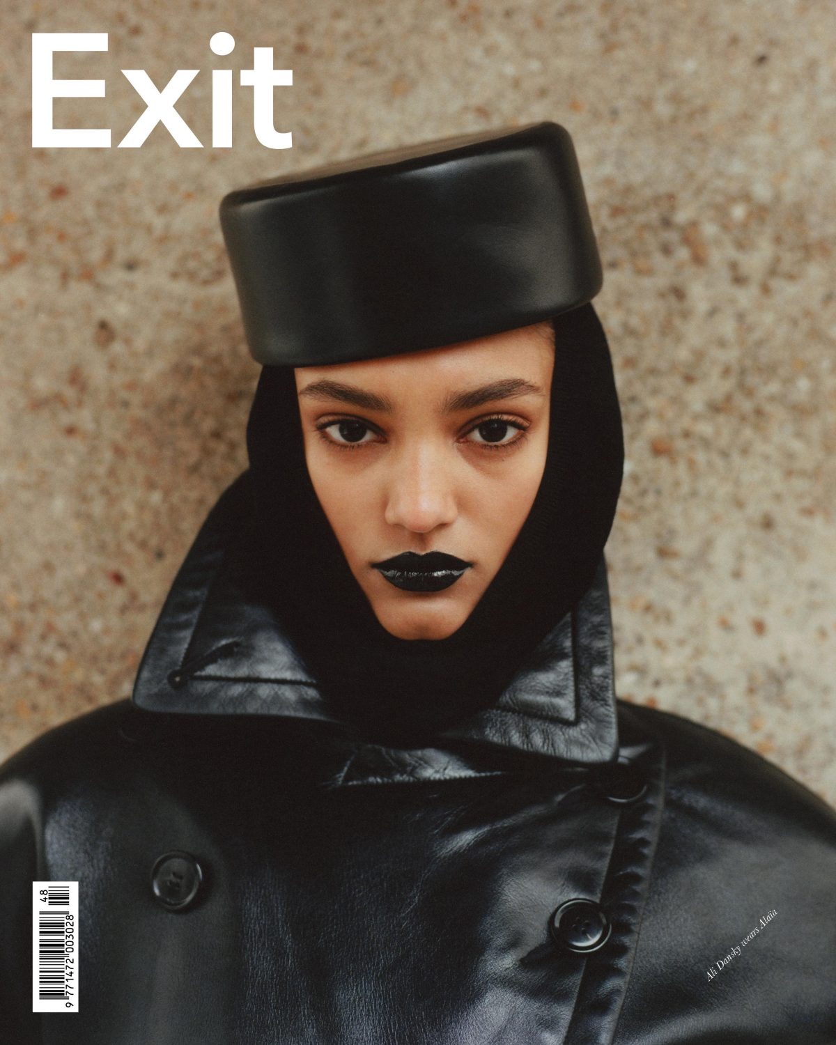 Magazine cover featuring a model with dark lipstick wearing a black leather coat and hat against a textured beige background.