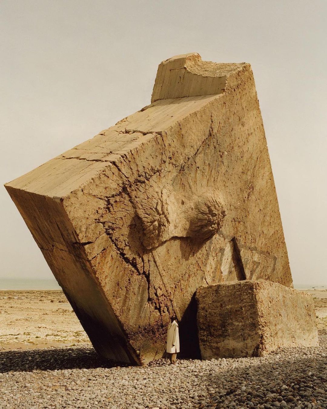 Abstract outdoor shot featuring a large, geometric block structure, resembling a weathered breast, with a human figure for scale.