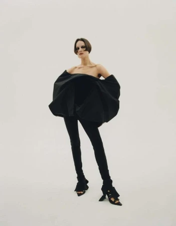 Model in voluminous black strapless top and slim trousers standing against a seamless white background