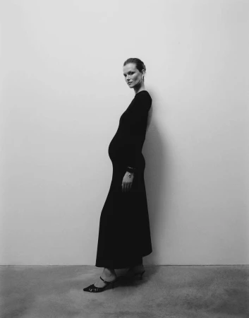 Pregnant woman in a long black dress standing against a neutral studio wall by photographers Kulesza and Pik
