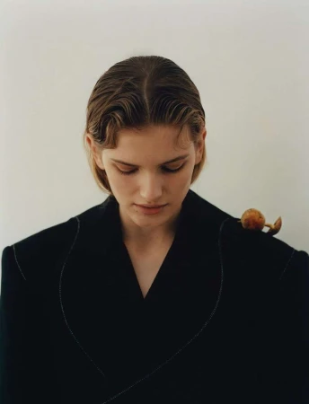 Close-up portrait of a woman with wet-look hair wearing a black blazer with a snail on her shoulder against a plain white background