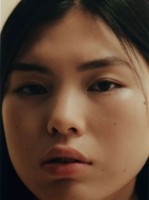 Close-up studio portrait of an East Asian young adult woman with dark hair, fair skin, and neutral expression.