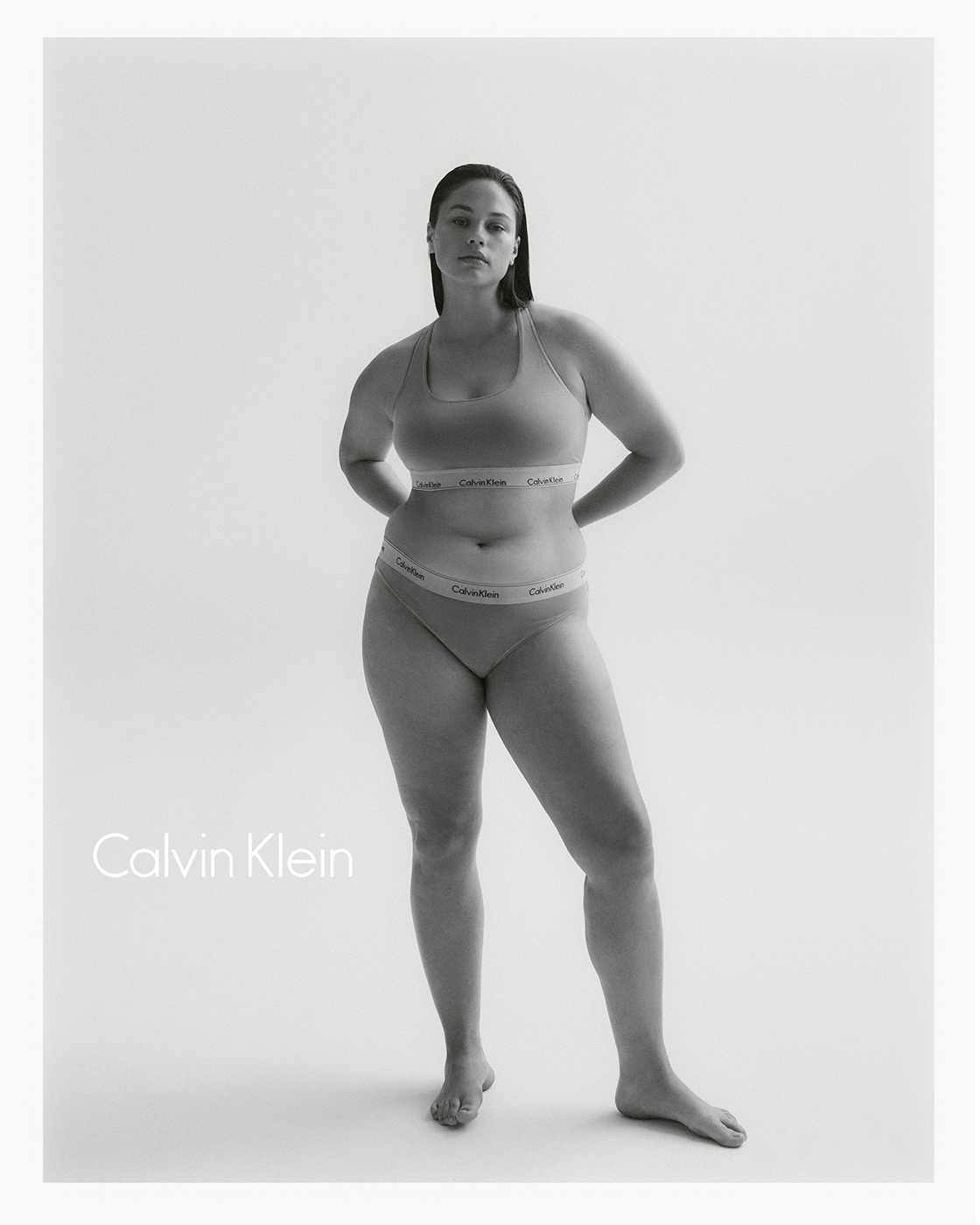 Monochrome studio shot of an adult woman posing in a Calvin Klein bra and underwear set against a bright white backdrop.
