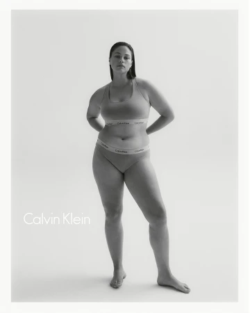 Monochrome studio shot of an adult woman posing in a Calvin Klein bra and underwear set against a bright white backdrop.