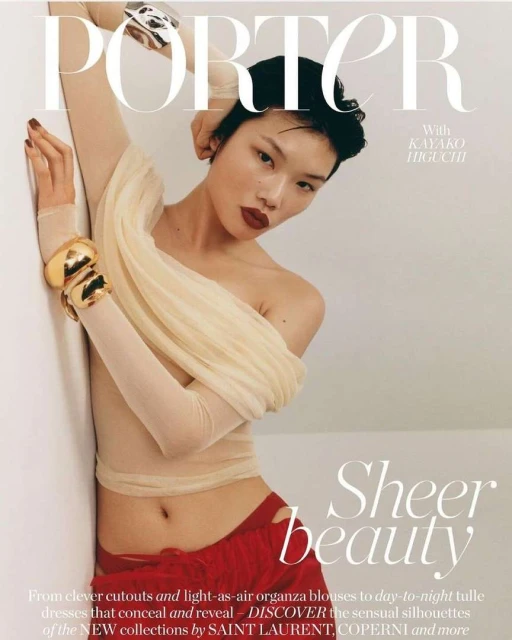 Magazine cover featuring a woman with short dark hair wearing sheer top and red pants, accessorized with gold bracelets, posing against a wall.